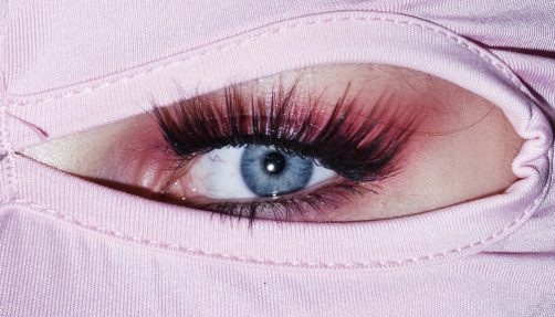 Fotografischer Bildausschnitt auf ein stark geschminktes Auge mit rosa Stoff, der das Gesicht um das Auge verdeckt