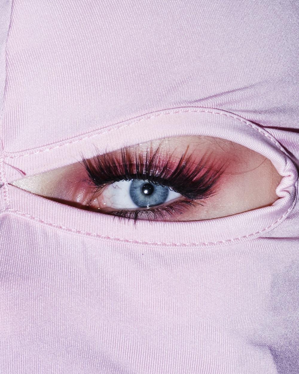 Fotografischer Bildausschnitt auf ein stark geschminktes Auge mit rosa Stoff, der das Gesicht um das Auge verdeckt