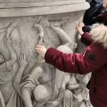 Tastführung in der "Enthüllt." Ausstellung. Frau ertasten den Sockel einer Statue.